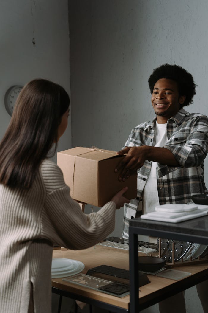 portfolio-03 A young man hands over a package to a woman in an indoor setting, symbolizing delivery services.